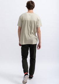 Lichtbeige katoenen t-shirt met een ronde hals en korte mouwen; gecombineerd met donkergroene broek en zwarte sneakers met witte zolen.