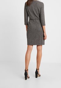 Grå knælang kjole med en struktureret vertikal mønster, trekvartærmer og en tætsiddende talje, parret med sorte højhælede sko.