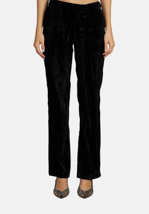 Pantaloni in velluto nero con taglio dritto, caratterizzati da una superficie testurizzata e una vita elastica. Abbinati a tacchi con punta aperta e decorazioni.