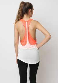 Top deportivo sin mangas con un diseño bicolor, parte superior naranja y sección inferior blanca, dobladillo redondeado y corte abierto en la espalda.