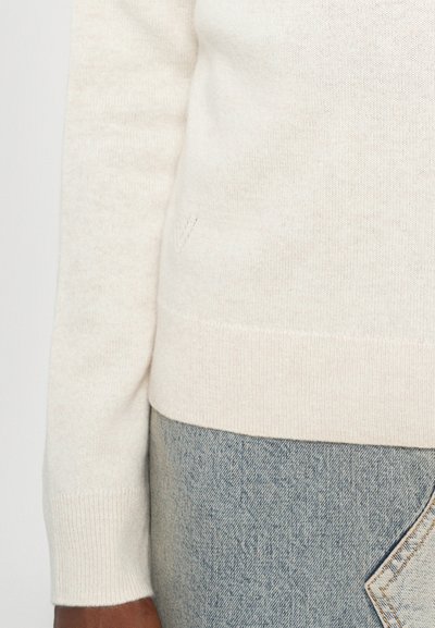 Cream knit sweater with a soft texture, fitted design, and ribbed cuffs and hem. Paired with light blue denim jeans featuring a pocket detail.