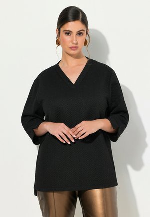 Top nero testurizzato con scollo a V e maniche 3/4, caratterizzato da un motivo a zigzag, abbinato a pantaloni marroni lucidi.