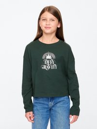 Zöld, hosszú ujjú, rövid cropped póló, amelyen egy fehér grafikai nyomtatás található, rajta a "DEFY GRAVITY" felirattal és kastély motívumokkal. Puha pamut anyag, laza szabás.