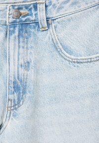 Jean en denim bleu clair en gros plan montrant la poche avant, la passants de ceinture et un bouton argenté avec des détails de couture orange.
