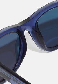 Ochelari de soare bleu marin cu un finisaj lucios, lentile rotunde și rame netede, curbe. Brațele subțiri și drepte de culoare neagră completează designul.