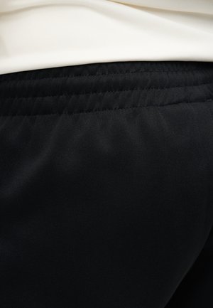 Κοντινό πλάνο μαύρης ελαστικής ζώνης σε παντελόνια με λευκό πουκάμισο που έχει μπει μέσα στην πάνω άκρη.