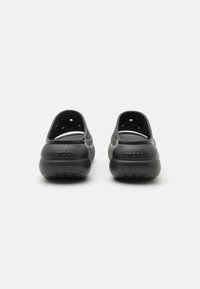 Svart Crocs klippfeller med en glatt tekstur, avrundet form, bakre hælstøtte og ventilasjonshull på sidene. Logo preget på hælen.