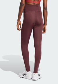 Burgundowe legginsy o wysokim stanie wykonane z elastycznego materiału, charakteryzujące się gładką fakturą i dopasowanym krojem, w połączeniu z białymi butami sportowymi.