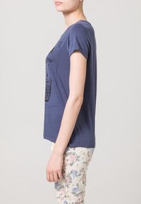 Tmavě modré tričko s krátkým rukávem a kulatým výstřihem, s grafickou potiskem na přední straně. Kombinováno s lehkými kalhotami s květinovým vzorem.