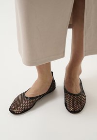 Balerini negri din plasă cu vârf rotund, talpă flexibilă și margine lucioasă. Materialul are un model de plasă mare, punând în evidență piciorul.