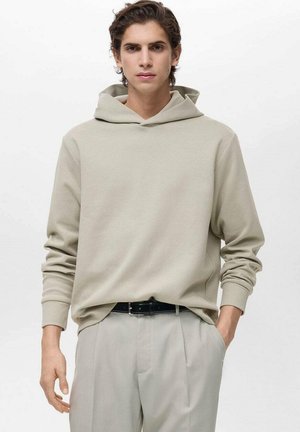 Lichtgrijze hoodie met een ruime capuchon en lange mouwen, gemaakt van zachte stof. Gecombineerd met lichtgrijze broek en een zwarte riem.