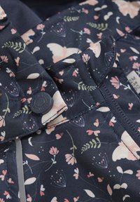 Marinblått tyg med ett blommönster som har rosa blommor och fjärilar. Inkluderar en kontrasterande knapp och sömnadsdetaljer för extra textur.