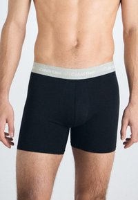 Fekete boxer alsónadrág szürke Calvin Klein derékgumival. Az anyag simának és rugalmasságnak tűnik, szoros illeszkedésre tervezve.