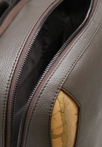 Zaino in pelle marrone con texture liscia. Presenta una chiusura con cerniera, una fodera interna e un dettaglio esterno con motivo a mappa.