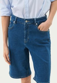 Zilas džinsu šorts ar taisnu griezumu, piecu kabatu dizainu, redzamu šuvju un priekšējo pogu aizdari. Gluda tekstūra.
