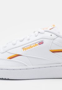 Sapatilha de couro branca com detalhes em laranja e amarelo, sola de borracha texturizada e logotipo da Reebok na lateral e na língua. Design clássico.