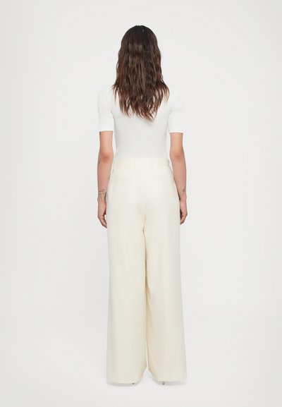 White fitted top paired with high-waisted cream wide-leg trousers. Smooth fabric, no visible patterns, two back pockets on pants.
