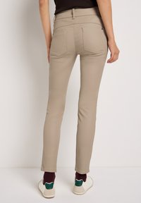 Pantalones ajustados beiges de tejido suave, pierna estrecha, con dos bolsillos traseros y sutiles detalles de costura, combinados con zapatos blancos y calcetines color burdeos.
