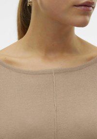 Haut en tricot beige avec un large col et un détail de couture central à l'avant. Texture lisse avec une finition fine et douce.