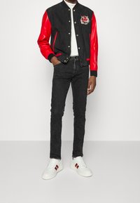 Svart och röd varsityjacka med tigerbroderi, matchad med svarta slim-fit jeans och vita sneakers med röda ränder.