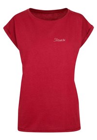 Rød bomulds t-shirt med korte, rullede ærmer og rund halsudskæring. Har hvid tekst med teksten "Det slår højt" på forsiden.