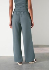 Lichte, wijde broek in een vervaagde teal stof. Heeft een elastische tailleband en zijzakken, met een gladde, zachte textuur.