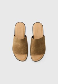 Sandales glissantes en suède marron avec un design à bout ouvert et une large bande sur le dessus. La semelle est beige avec un léger talon.