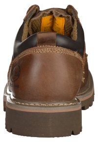 Botte de travail en cuir marron avec un col noir, une languette rembourrée, une semelle en caoutchouc avec des crampons pour l'adhérence et des détails de coutures contrastés.