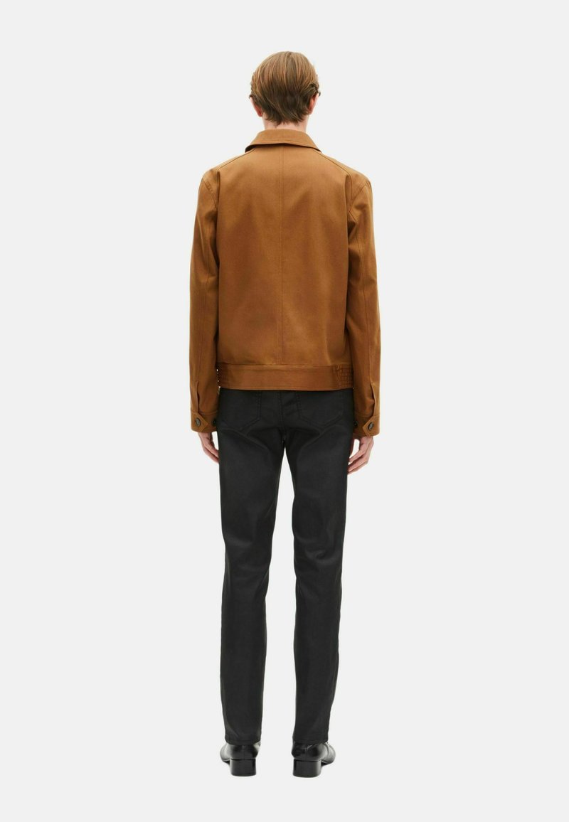 Veste en cuir marron avec un col classique, design simple, finition texturée et jeans noirs, vue de derrière. Des chaussures noires sont portées.