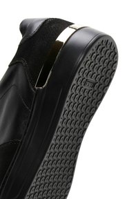 Baskets en cuir noir avec un dessus texturé, un accent doré métallique au talon et une semelle en caoutchouc gris avec un motif de grip.