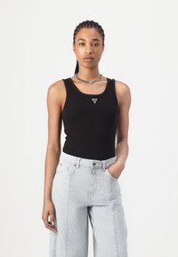 Svart ribbet tanktopp med rund hals og en liten logo på midten av brystet, kombinert med høytlivede lyse stripete jeans.