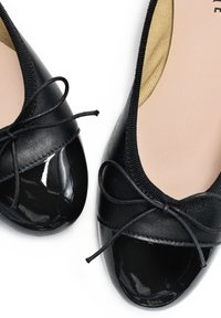 Ballerine nere in pelle con punta in vernice lucida, caratterizzate da un fiocco decorativo e una morbida fodera interna.