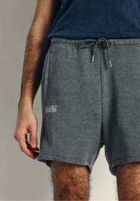 Pantalones cortos de algodón grises con cintura elástica y cordón de ajuste, con bolsillos laterales y un parche con el logo que dice "American Vintage."
