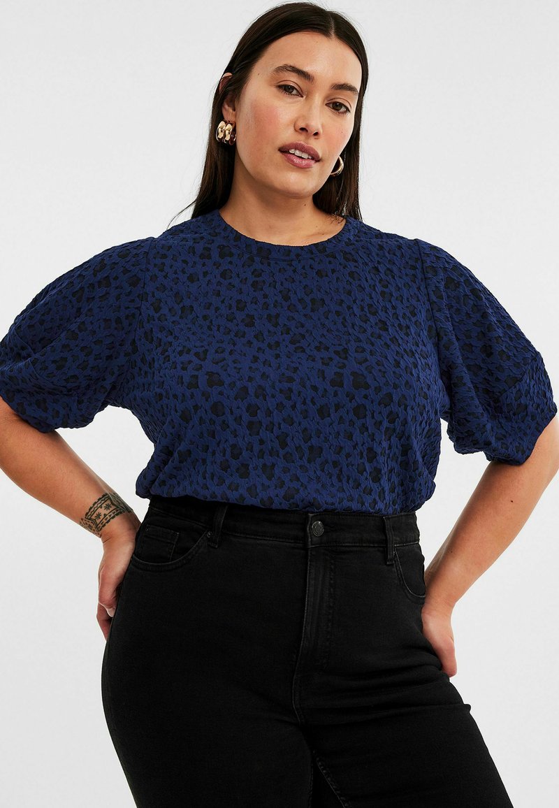 Mörkblå kortärmad topp med en strukturerad leopardmönster; rund halsringning och avslappnad passform, kombinerad med högmidjade svarta jeans.