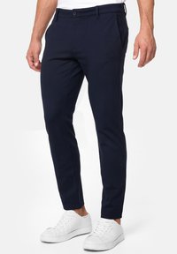 Mornarsko plavi slim-fit chinos hlače izrađene od lagane mješavine pamuka, s ravnim prednjim dijelom, dva bočna džepa i kopčanjem na gumbe. Uparene s bijelim tenisicama.