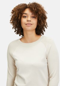 Cremiger Pullover mit gerippten Ärmeln und rundem Halsausschnitt. Weicher Stoff, enganliegende Form und lange Ärmel. Einfaches Design in neutraler Farbe.