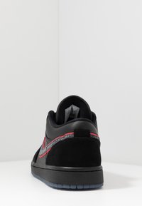 Baskets noires avec une tige en daim, des accents rouges et une semelle en caoutchouc. Dotées d'un col rembourré et d'un design cousu sur le côté.