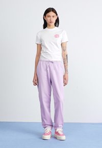 Hvit kortermet t-skjorte med rosa grafikk og lilla joggebukser med elastisk midje, kombinert med rosa og hvite joggesko.