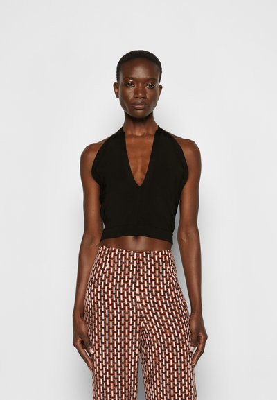 Top cropped preto, estilo halter, com decote em V profundo, combinado com calças largas estampadas com um padrão geométrico em castanho e branco.