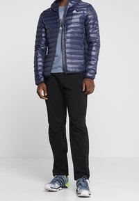 Marinblå pufferjacka med huva, texturerat tyg, dragkedjestängning. Bärs över en ljusblå grafisk t-shirt, ihop med svarta byxor och grå sneakers.