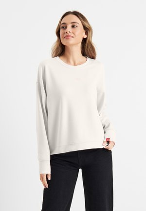 Lichtbeige sweatshirt met een ronde hals en verlaagde schouders. Heeft een subtiele roze logo op de borst en een rode label op de mouw.