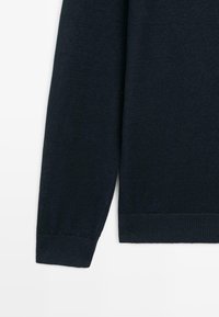 Langærmet mørkeblå strikket sweaterærme og side, der viser ribbet manchet og kant på hvid baggrund.