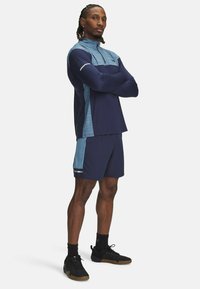 Marineblauw sportshirt met blauwe accenten, kraag met kwartrits en korte mouwen, gecombineerd met bijpassende marineblauwe shorts en zwarte sneakers.