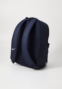 Mochila azul-marinho com alças acolchoadas ajustáveis, apresenta um pequeno logótipo branco e um bolso lateral, feita de tecido resistente com textura suave.