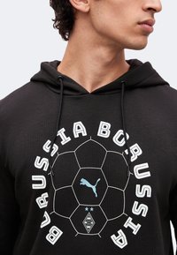 Άτομο που φοράει μαύρη κουκούλα Borussia με λευκό σχέδιο ποδοσφαίρου και το λογότυπο της Puma στο κέντρο.