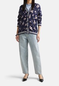 Marinblå cardigan med blommönster, vita ränder och knappar, som matchas med en ljusblå skjorta och glittriga ljusblå jeans. Svarta klackar.