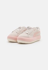 Baskets en daim beige clair avec semelles compensées en caoutchouc rose, logo Puma rose et lacets, présentées côte à côte sur un fond blanc.