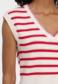 Bezrękawnik dzianinowy w białe i czerwone poziome paski oraz dekoltem w serek z czerwonymi detalami na osobie z widokiem na górną część tułowia.