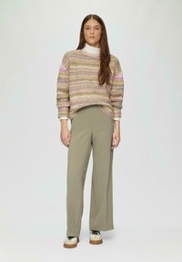 Multikleurige gebreide trui met roze, groene en witte strepen, gecombineerd met licht olijfgroene wijde broek en sneakers met beige accenten.