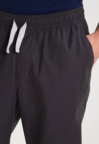 Mörkgråa träningsoverallsbyxor med resårmidja, försedd med en vit dragsko och sidofickor. Slät textur och minimalistisk design.